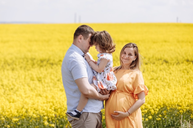 Glückliche schwangere Familie mit der kleinen Tochter, die Zeit zusammen in einem gelben Rapsfeld am Sommertag verbringt