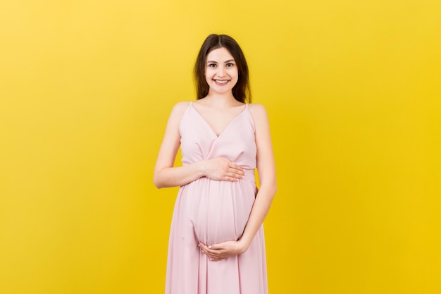 Glückliche schwangere Frau berührt ihren Bauch am farbigen Hintergrund zukünftige Mutter Erwartet ein Baby Kopieren Sie den Raum