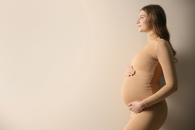 Glückliche schwangere Frau, die ihren Bauch auf beigem Hintergrund berührt Platz für Text