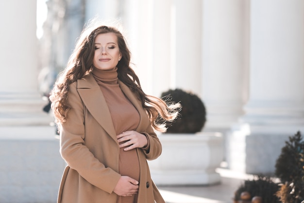 Glückliche schwangere Frau, die stilvolle Jacke und Kleid trägt