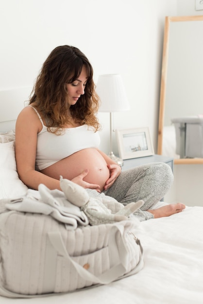 Glückliche schwangere Frau, die zu Hause sitzt und ihren Bauch berührt