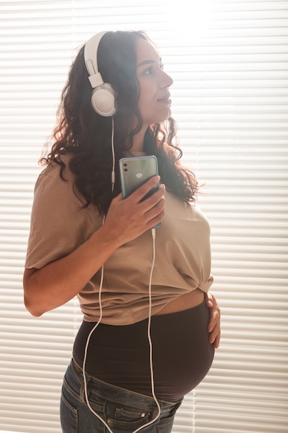 Foto glückliche schwangere frau mit dem lockigen haar, das musik in den kopfhörern hört