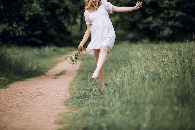 Foto glückliche schwangere frau mit einem blumenstrauß, der barfuß auf dem gras läuft