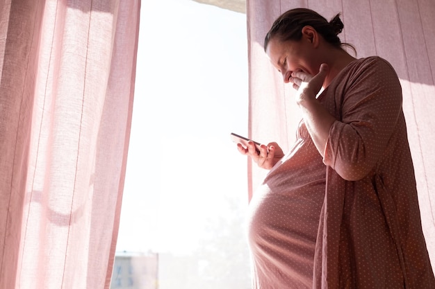 Glückliche schwangere kaukasische Frau, die sms lächelnd liest