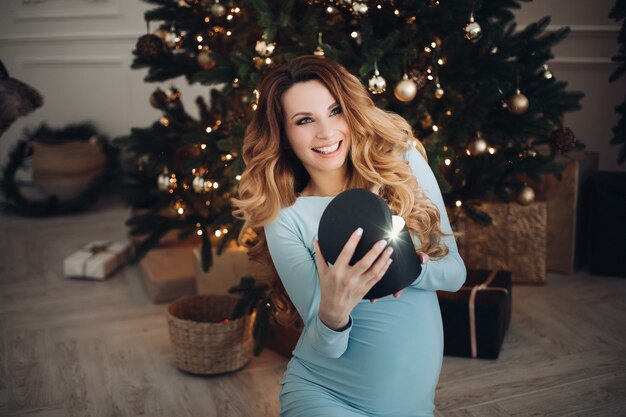 Glückliche Schwangerschaftsfrau, die ein Weihnachtslichtgeschenk mit positiver Emotion öffnet