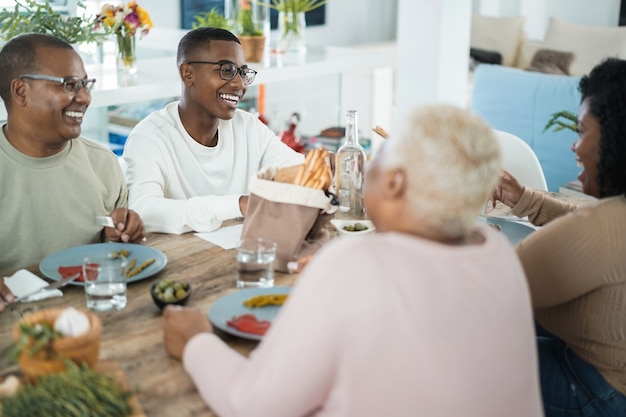 Glückliche schwarze Familie, die zu Hause zu Mittag isst - Vater, Tochter, Sohn und Mutter, die zusammen Spaß am Esstisch haben - Hauptfokus auf Sohngesicht