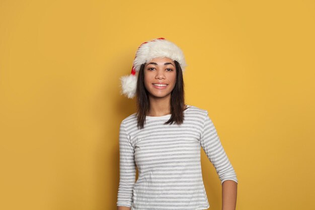 Glückliche schwarze Frau mit Weihnachtsmannshut lächelt auf gelbem Hintergrund