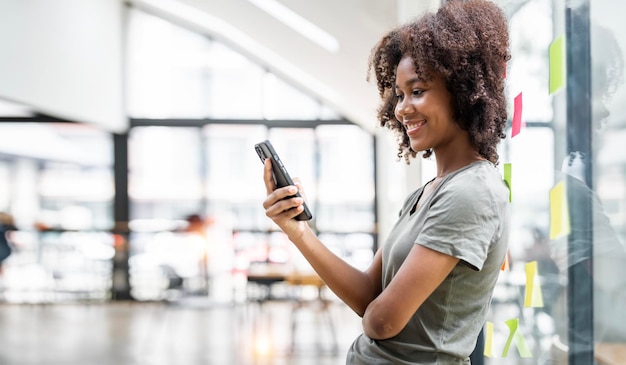 Glückliche schwarze Geschäftsfrau mit einem Smartphone in einem Kreativbüro