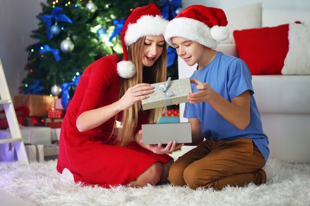 Glückliche Schwester und Bruder öffnen Geschenkbox auf dem Boden im dekorierten Weihnachtsraum