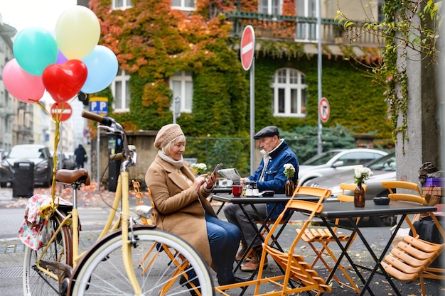 Glückliche Senioren sitzen im Straßencafé in der Stadt und benutzen Smartphone.