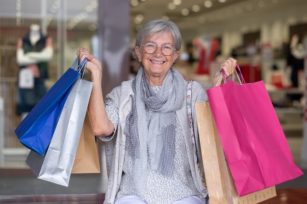 Glückliche Seniorin, die Einkaufstaschen trägt und das Einkaufskonzept des Konsumkundenverkaufs genießt