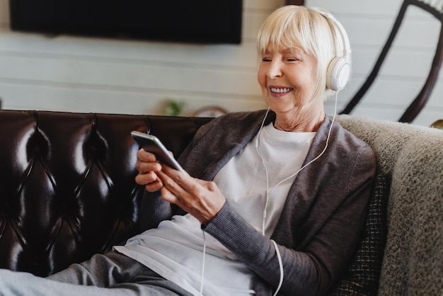 Glückliche Seniorin mit Kopfhörern, die zu Hause Musik hört