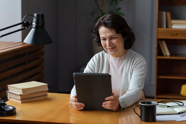 Glückliche Seniorin mittleren Alters, die ein Tablet-Gespräch über einen Videoanruf mit der Familie von Freunden hält