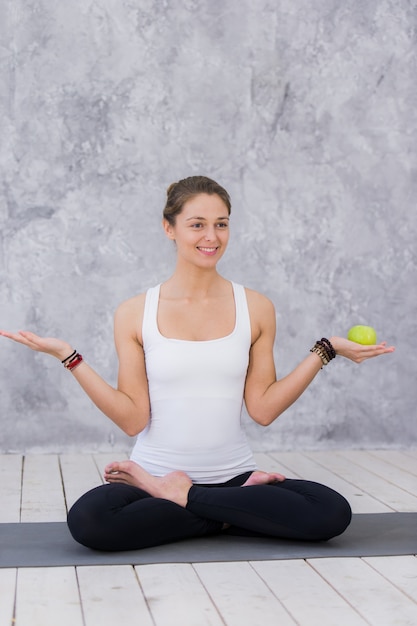 Glückliche Sportfrau, die Apfel hält auf einer Yogamatte hält