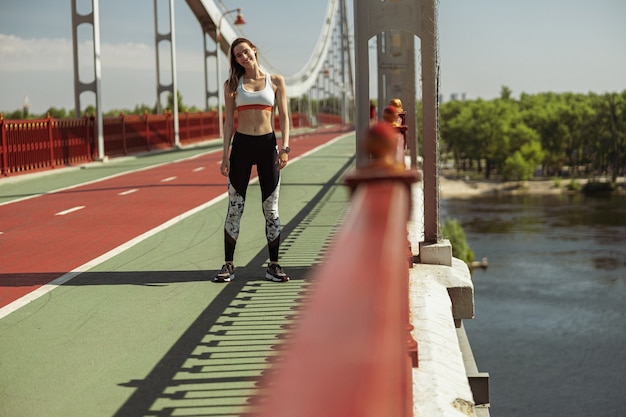 Glückliche sportliche Frau in moderner Sportkleidung posiert für die Kamera auf der Fußgängerbrücke