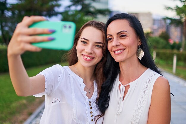 Foto glückliche stilvolle attraktive lächelnde tochter mit mutter nehmen selfie-fotoporträt auf telefonkamera, während sie zusammen draußen gehen