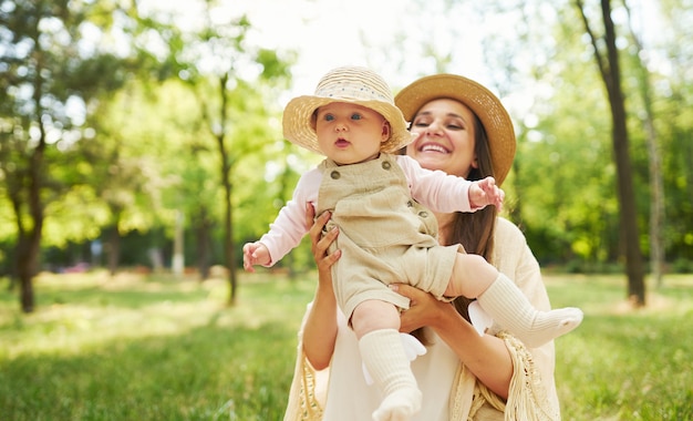 Glückliche stilvolle und liebevolle Familie. Mutter spielt mit ihrem Baby im Freien. schönes Baby lächelt und genießt. Muttertagskonzept.