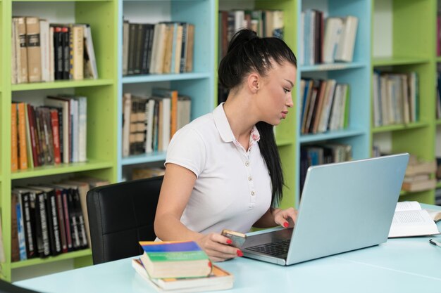 Glückliche Studentin, die mit Laptop in der Bibliothek arbeitet