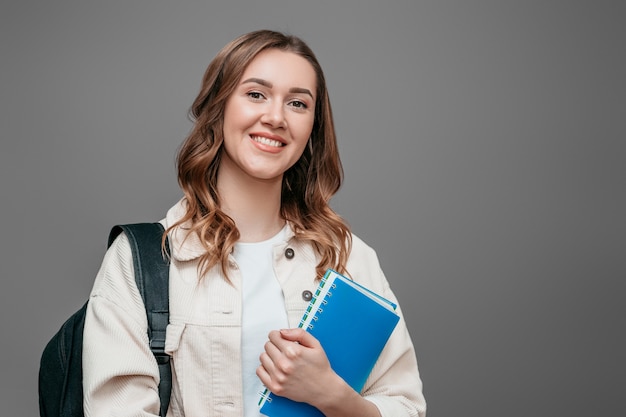 Glückliche Studentin mit Rucksack ein Notizbuch lächelt isoliert über dunkelgrauem Wandwebbanner. Das Konzept der Bildung lernen Englisch