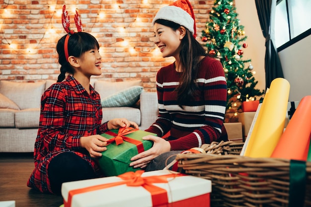 glückliche süße Familie Verpackung Weihnachtsgeschenkboxen wunderbare Teamarbeit, die gemeinsam Kunstdesign macht. verpackungsgeschenk für weihnachten und neujahr in der nähe von baum. voller bunter Papierhandwerke und Bänder im Korb.