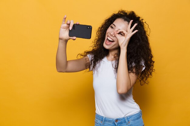 Glückliche süße junge Frau posiert isoliert auf Gelb machen ein Selfie mit dem Handy