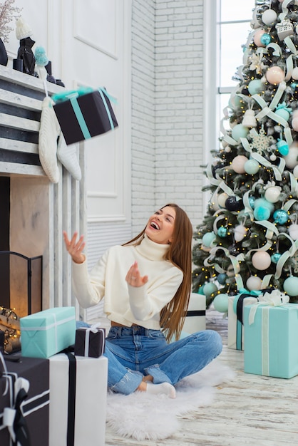 glückliche süße junge frau wirft zu weihnachten zu hause geschenk auf