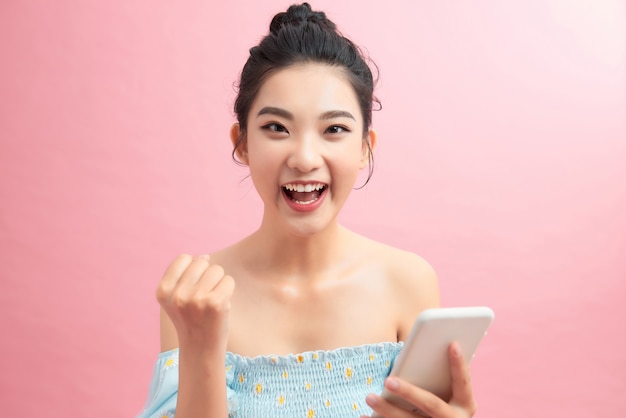 Glückliche süße schöne junge Frau spielt Spiele mit dem Handy auf rosa Hintergrund.