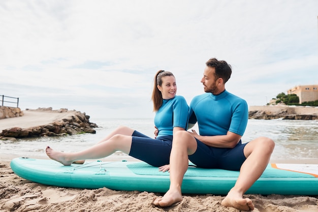 Glückliche Surfer sitzen auf dem Paddle Board am Strand