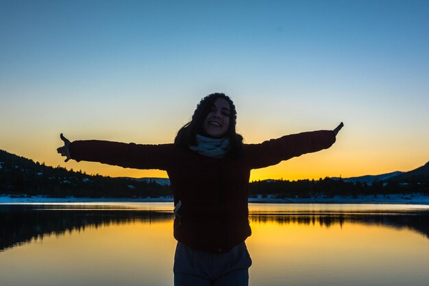 Foto glückliche teenager, die bei sonnenuntergang am see gegen einen klaren himmel stehen