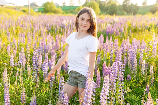 Glückliche Teenager-Mädchen lächelnd im Freien. Schöne junge jugendlich Frau, die auf Sommerfeld mit blühendem grünem Hintergrund der wilden Blumen stillsteht. Freies glückliches Kind Teenager Mädchen Kindheit Konzept