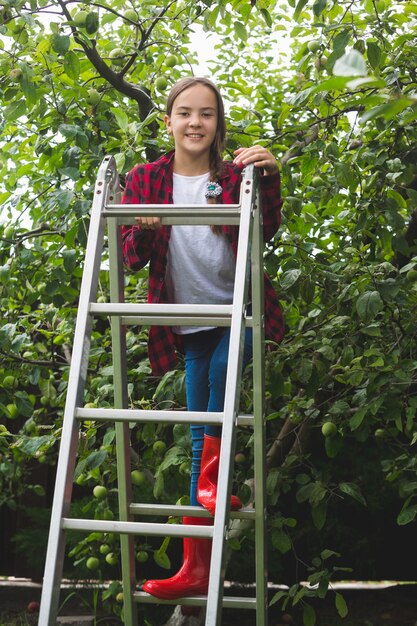 Glückliche Teenager-Mädchen posiert auf Trittleiter im Apfelgarten
