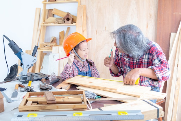 Glückliche Tischlerfamilie. Das kleine Mädchen und ihr Großvater heben Ihre Hände, während sie in einem Holzladen an Holzarbeiten arbeiten.