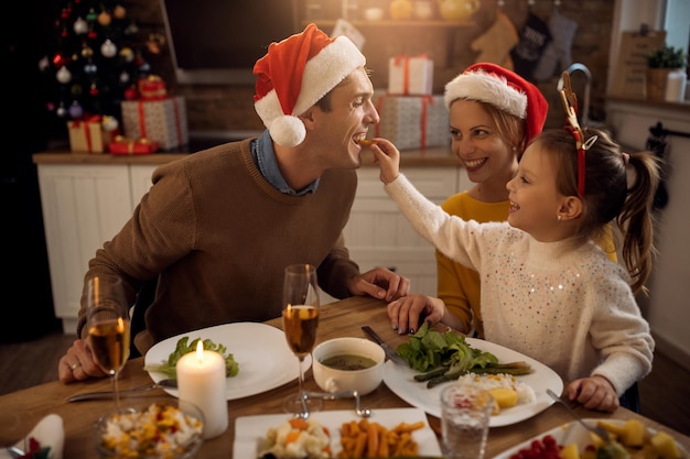 Glückliche Tochter, die ihren Vater während des Familienessens am Weihnachtstag füttert