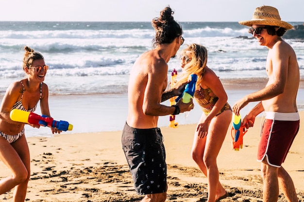 Glückliche Touristen amüsieren sich am Strand beim Spielen mit Wasserpistolen Junge Männer und Frauen genießen den Sommerurlaub und lachen gemeinsam in Freundschaft Ozean und Küste im Hintergrund