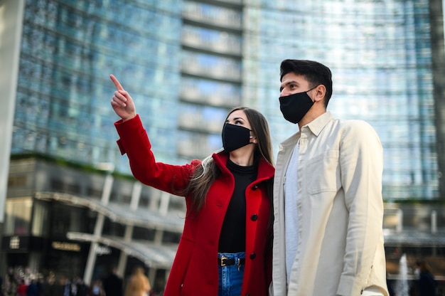 Glückliche Touristen mit Covid- oder Coronavirus-Masken paaren zusammen in einer Stadt und sehen einen interessanten Ort