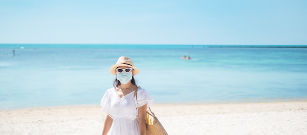 Glückliche Touristenfrau, die chirurgische Gesichtsmaske trägt, genießen schönes Meer und weißen Sand