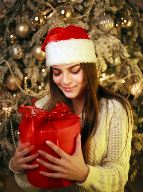 Glückliche träumerische Frau mit Geschenk zu Hause auf Baumdekorationen des neuen Jahres