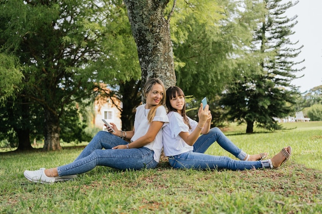 Glückliche und entspannte Mutter und Tochter, die Rücken an Rücken im Park sitzen.