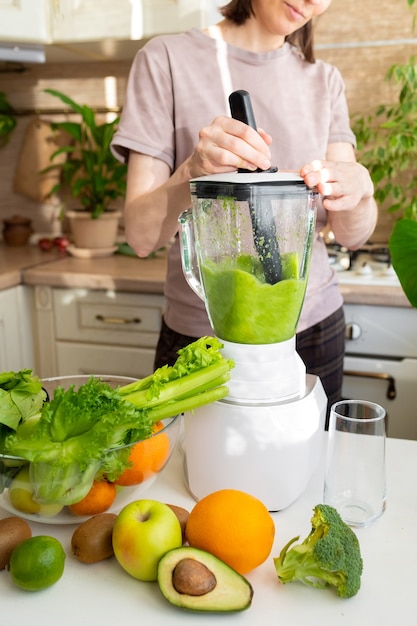 Glückliche und fröhliche kaukasische Frau in einem T-Shirt in ihrer Küche macht einen grünen Smoothie