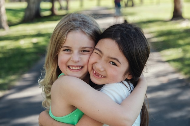 Glückliche und gesunde gemischte ethnische junge kleine Mädchen, die im Park, in den besten Freunden und in der Freundschaft umarmen und lächeln