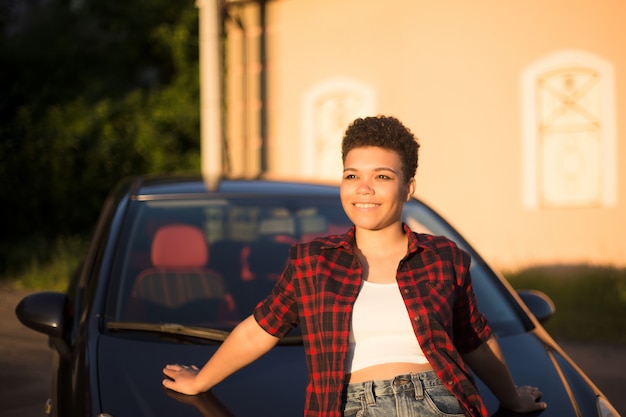 Glückliche und schöne Afroamerikanerin mit kurzen Haaren in der Nähe des Autos, Lebensstil.