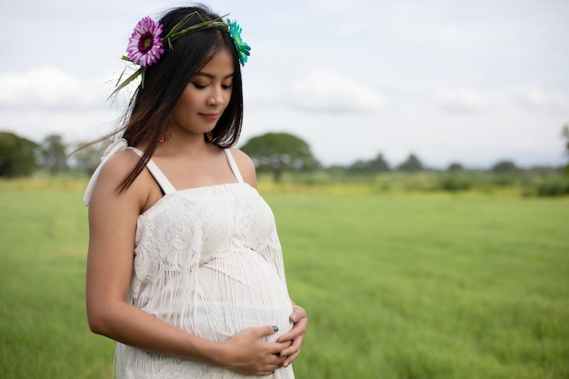 glückliche und stolze schwangere asiatische Frau, die ihren Bauch in einem Park bei Sonnenaufgang betrachtet