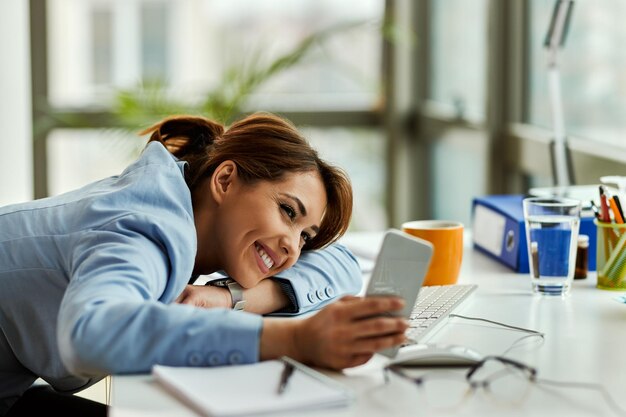 Glückliche Unternehmerin, die Smartphone und Textnachrichten verwendet, während sie sich im Büro entspannt