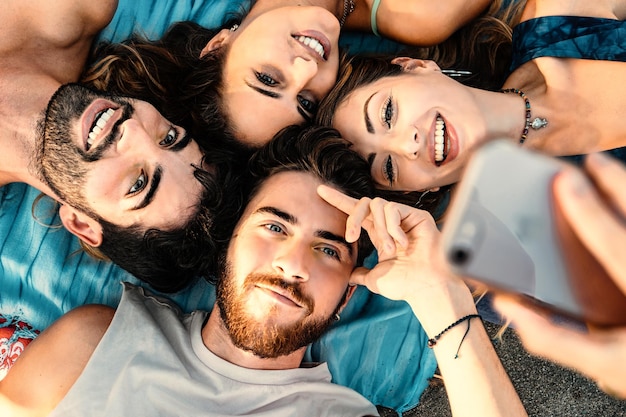 Glückliche vereinte Freunde, die sich am Strand hinlegen und ein Selfie machen