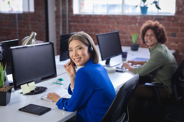 Glückliche, vielfältige männliche und weibliche Kollegen, die mit Headsets vor Computern sitzen