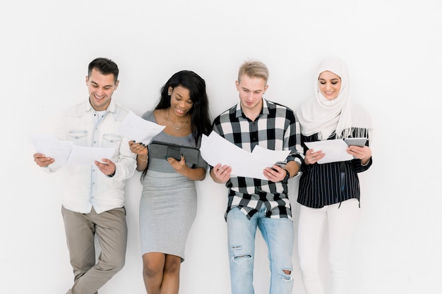 Glückliche vier verschiedene Freunde, die zusammen lernen, lächelnde Kerle und Mädchen