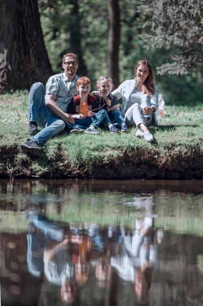 Foto glückliche vierköpfige familie, die auf dem gras auf dem see sitzt