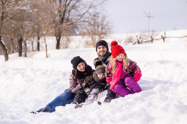 Glückliche vierköpfige Familie, die im Schneewald sitzt