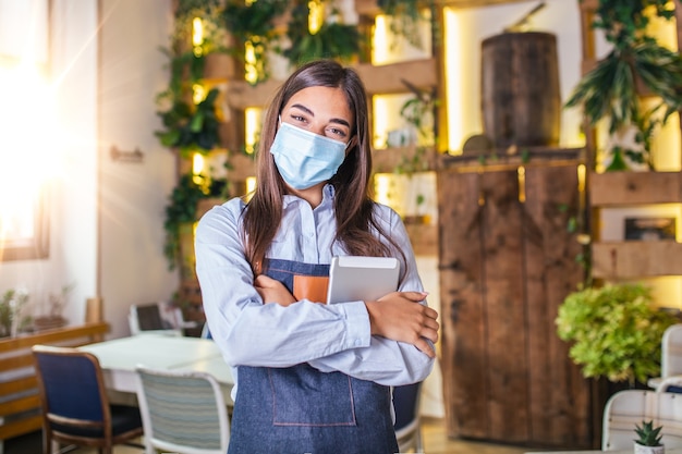 Glückliche weibliche Kellnerin mit digitalem Tablet beim Tragen einer Gesichtsschutzmaske im Restaurant oder Café. Nach dem Sperren aufgrund des Ausbruchs des Coronavirus covid-19, New normal, wieder öffnen