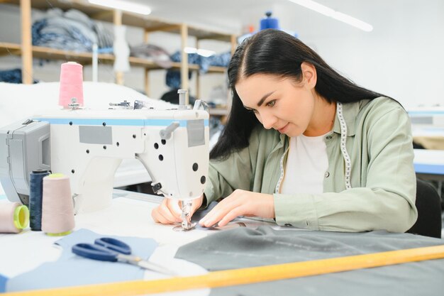 Glückliche weibliche Schneiderin, die mit Nähmaschine in der Textilfabrik arbeitet